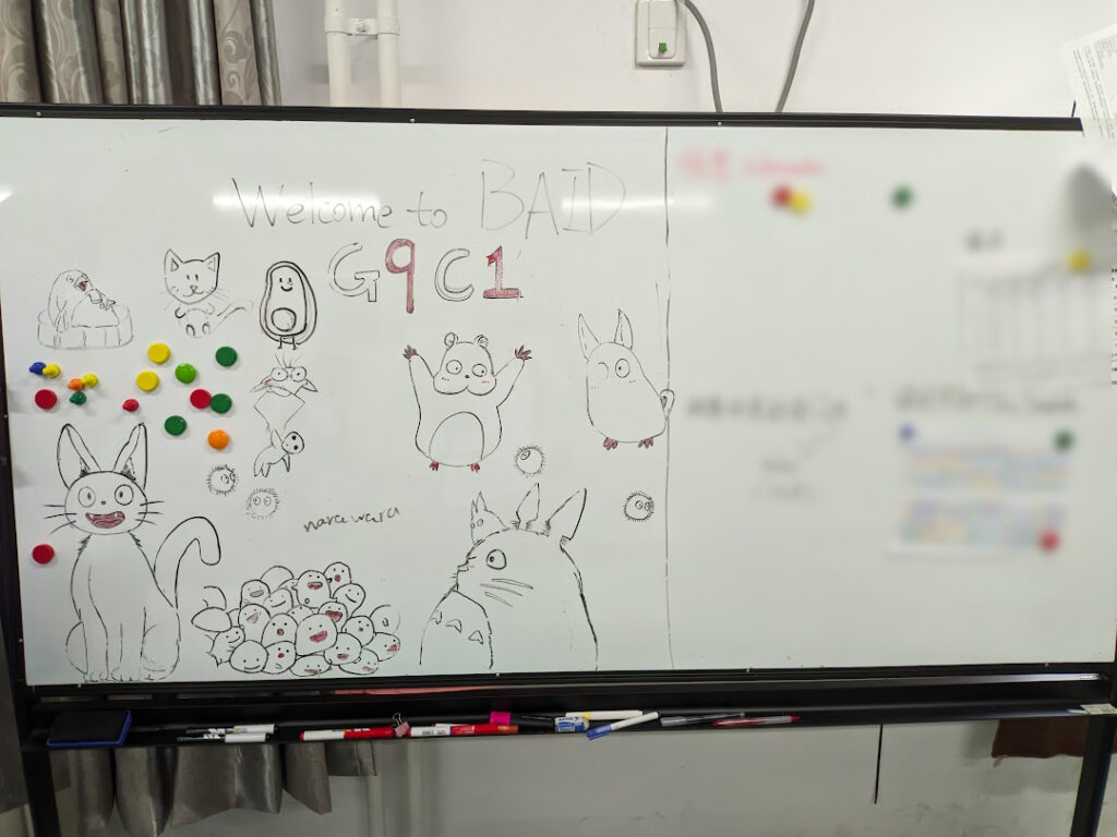 A whiteboard with the text "Welcome to BAID" and "G9C1" on it, along with drawings of anime characters.