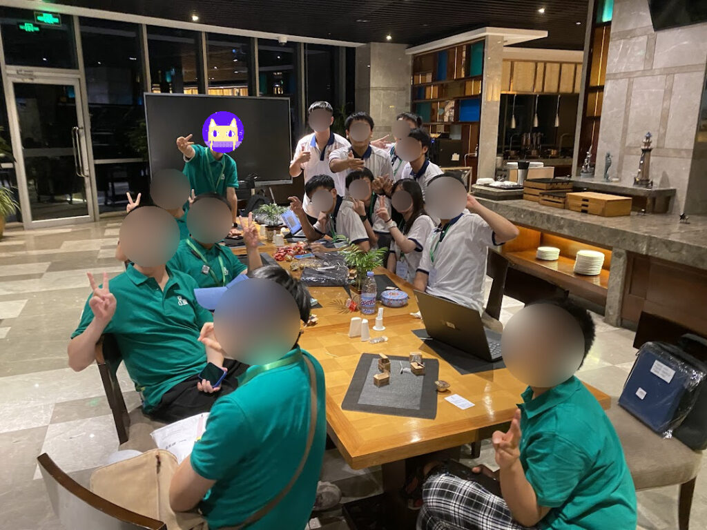 Students posing for a group photo around a hotel table at night. Students wearing green are from Beijing and students wearing white are from Macao.