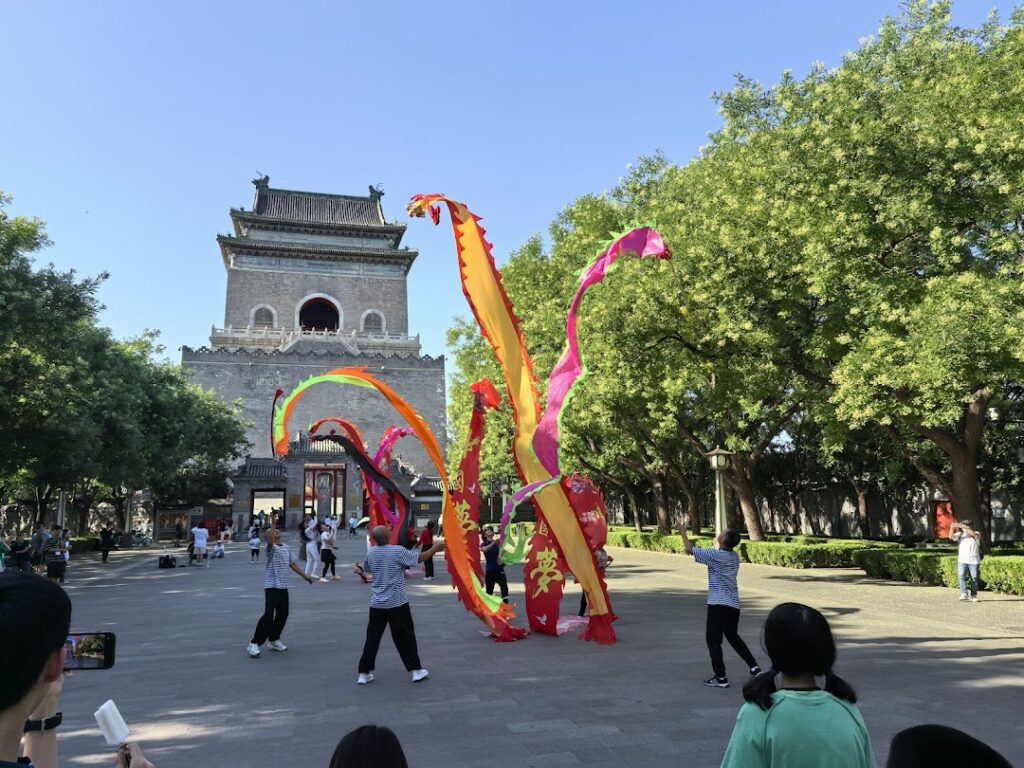 On a sunny afternoon, students between Beijing and Macao gather around to see a wuloong (dancing loong) performance before Beijing's Zhonglou (Clock Tower).