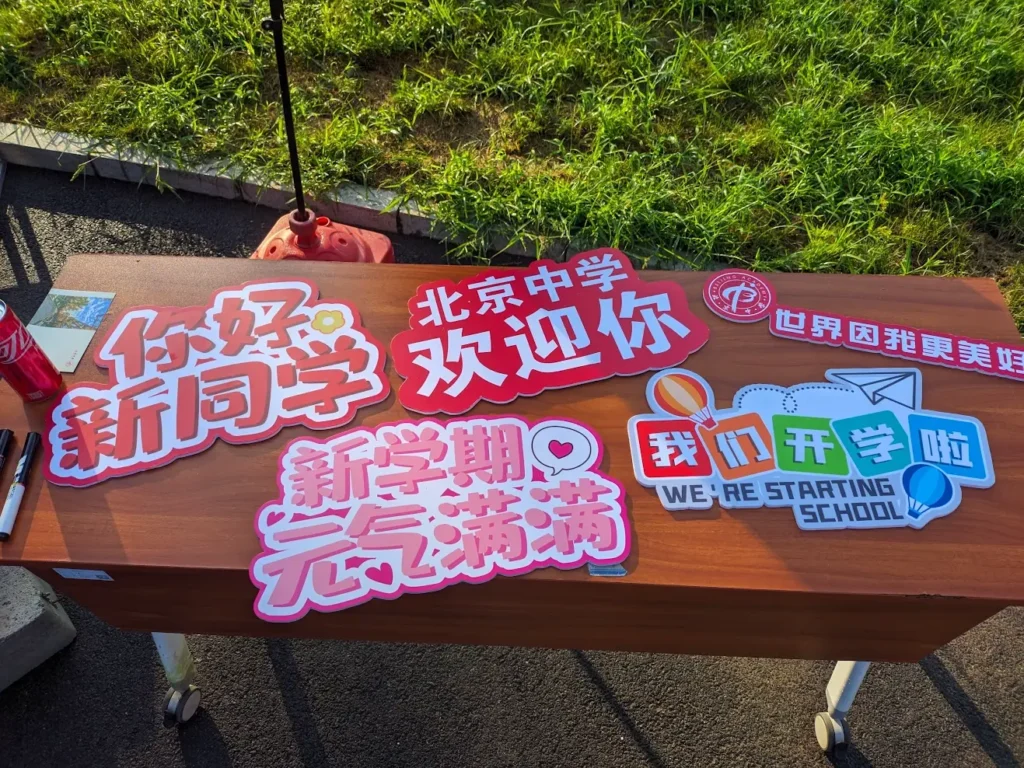 A table with several boards for photo-shooting on it. The boards read, "Hello freshman!," "We're starting school," "Better me, better world," "Welcome to Beijing Academy," "Have a fun new semester"