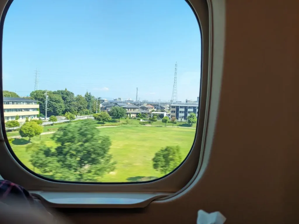 The window of the Shinkansen, outside of which is grass under the blue sky.