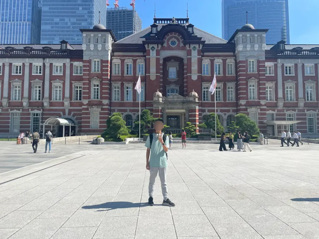 A teenage boy in front of the signature view of Tokyo station, the red building.