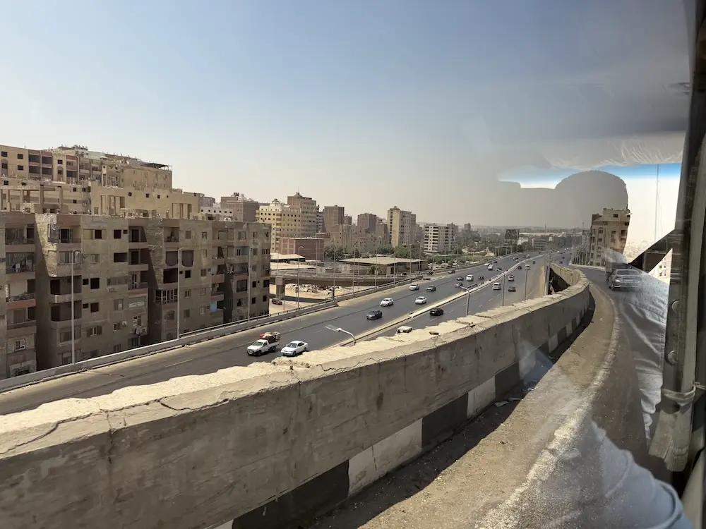 Taken outside a car window of an Egyptian highway. Sand-colored, windowless houses line up next to the road.