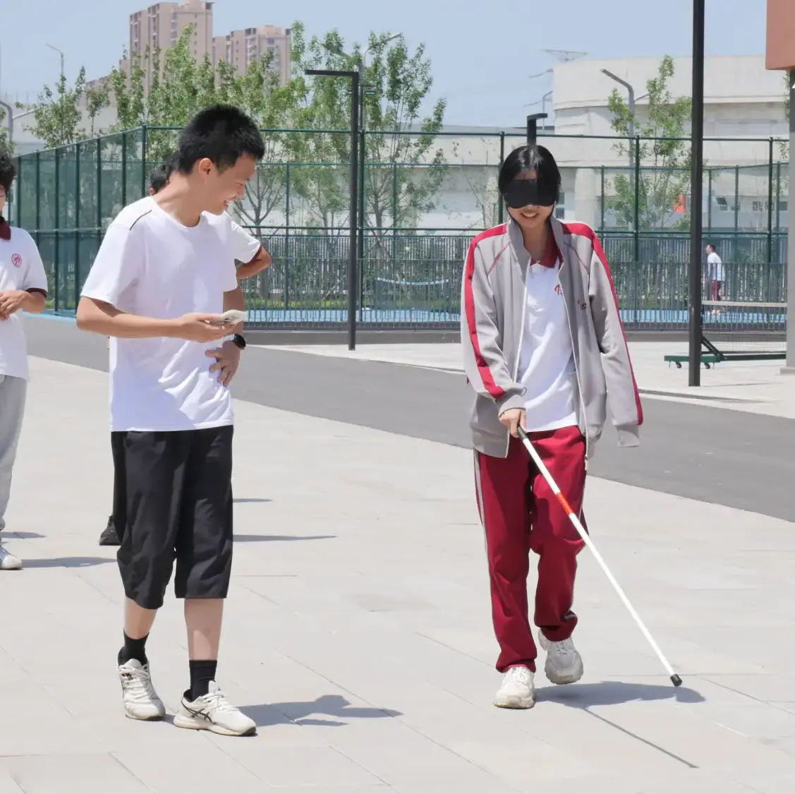 Lin smiling while guiding a female blindfolded student using a white cane.
